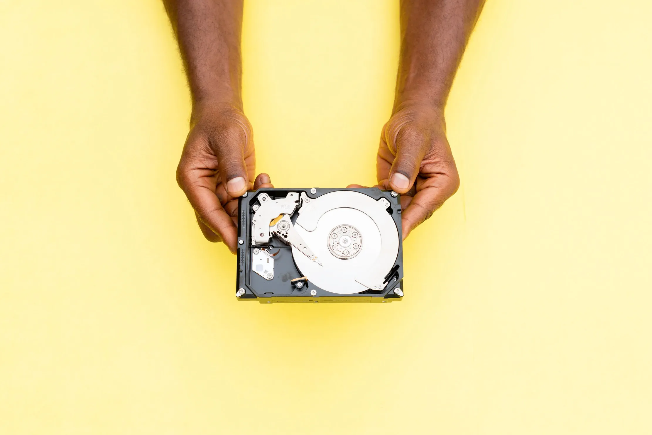Hands placing a hard drive into a protective case while other computers sit on a workbench