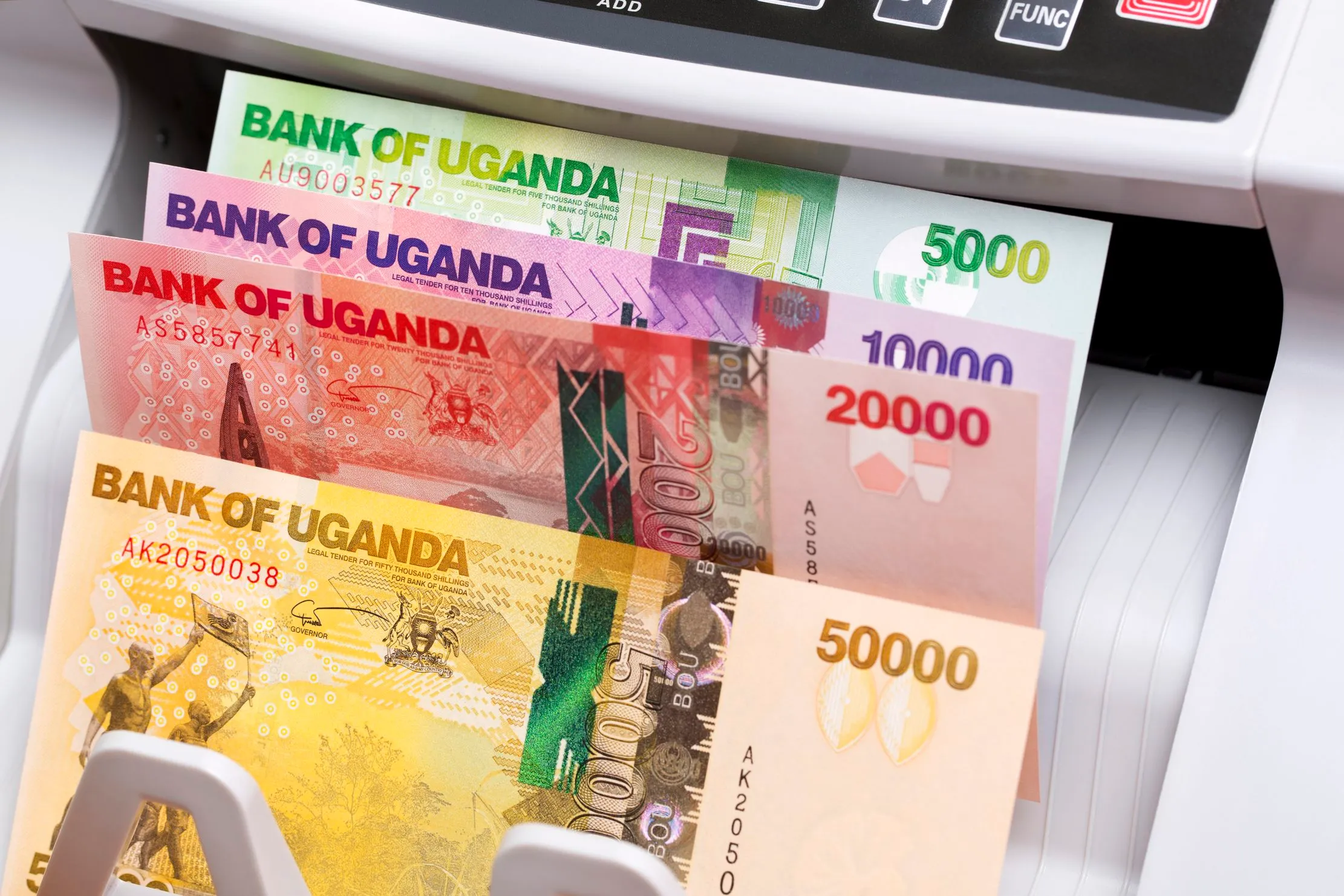 Ugandan shilling notes in a counting machine, representing local-currency settlement and reporting