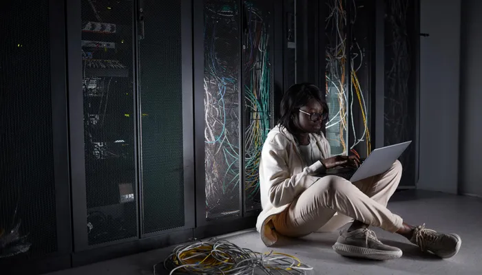 Woman using a laptop beside server racks, representing a digital service designed for constrained connectivity
