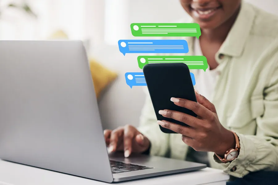 Personne utilisant téléphone et ordinateur pour communiquer avec un client, symbole du passage humain depuis un assistant IA WhatsApp